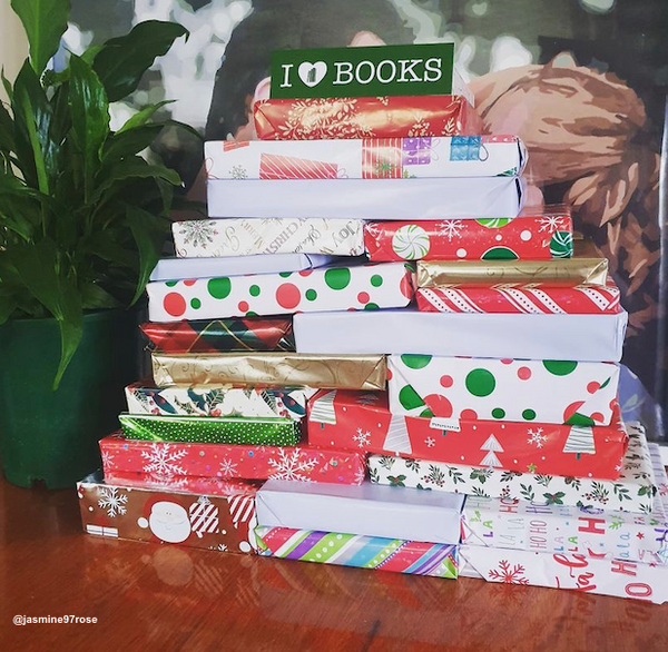 Image shows 24 individually wrapped books in festive patterns, in a stack that resembles the shape of a Christmas tree. It is topped with a bookmark that says 